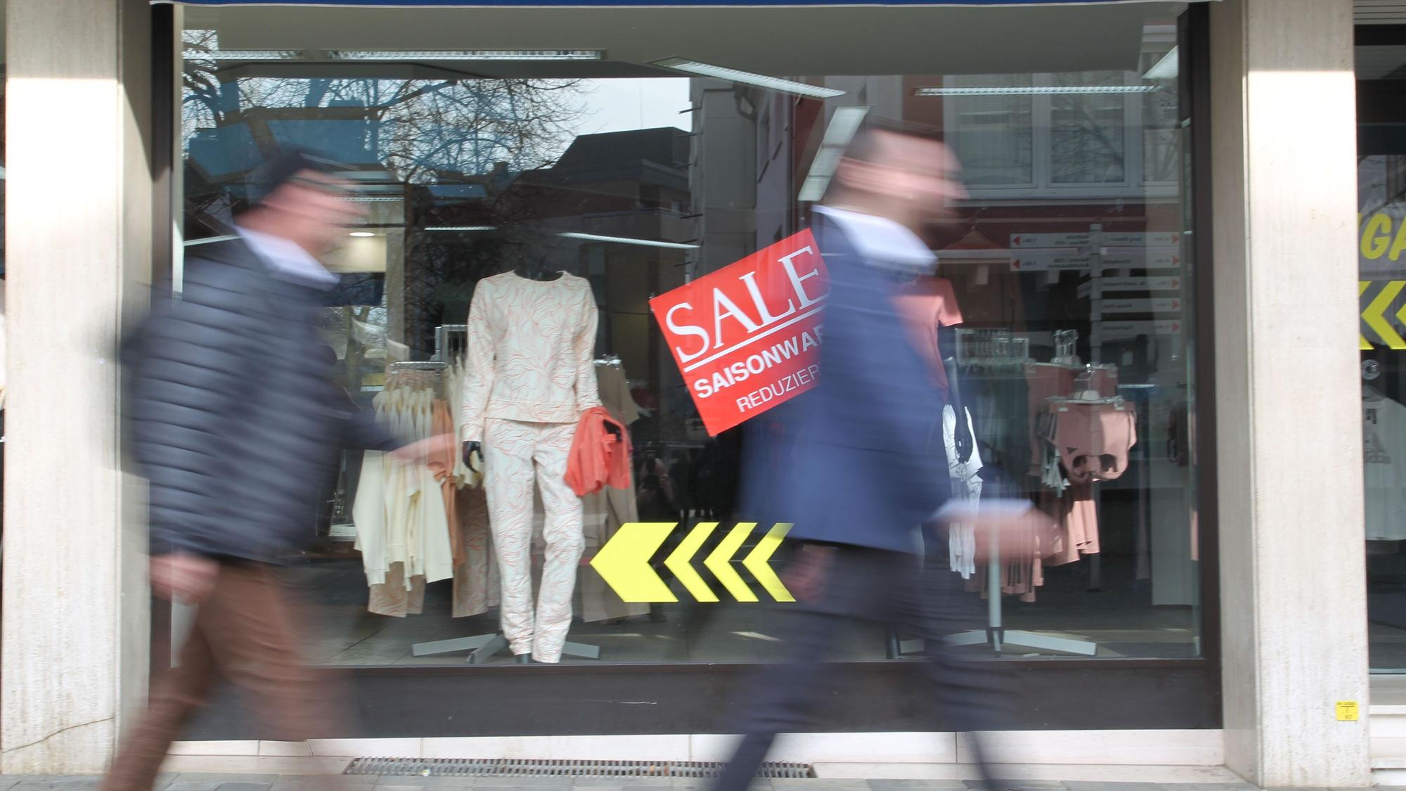 Zwei Männer gehen an einem Schaufenster vorbei.