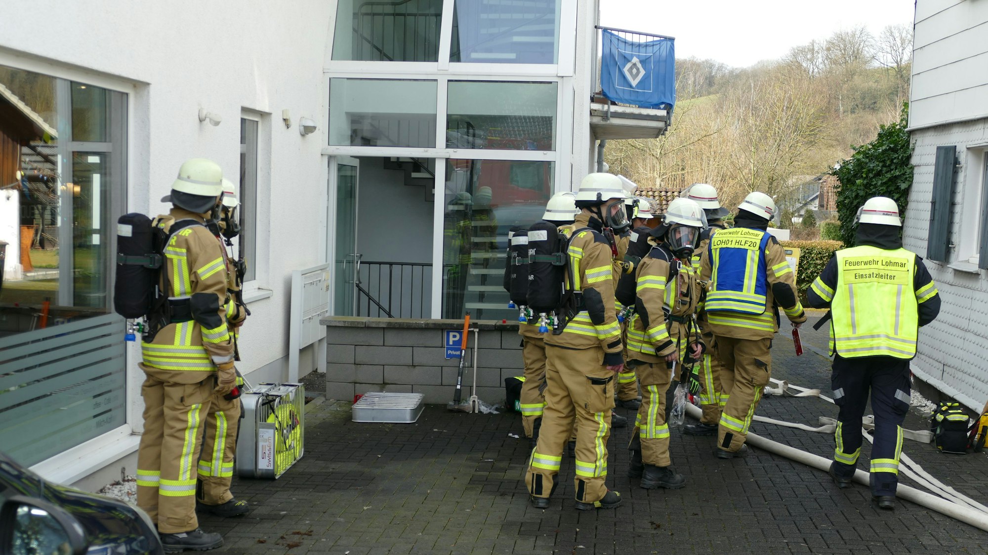 Mehrere Feuerwehrleute mit Helmen und Atemschutzmasken an einem Wohnhaus.