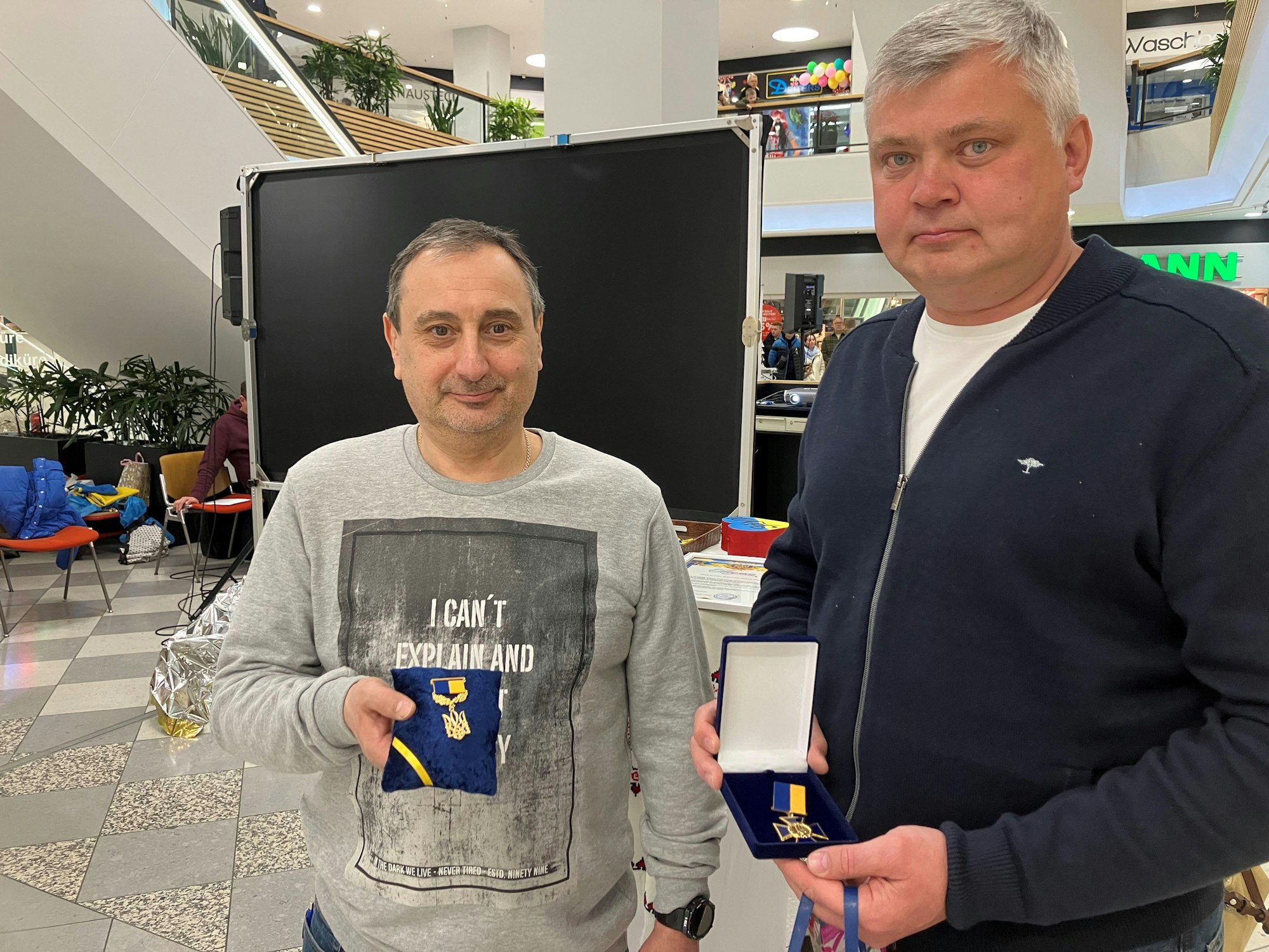 Zwei Männer stehen nebeneinander und halten zwei ukrainische Wappen in den Händen, die sie als Dankeschön erhalten haben.