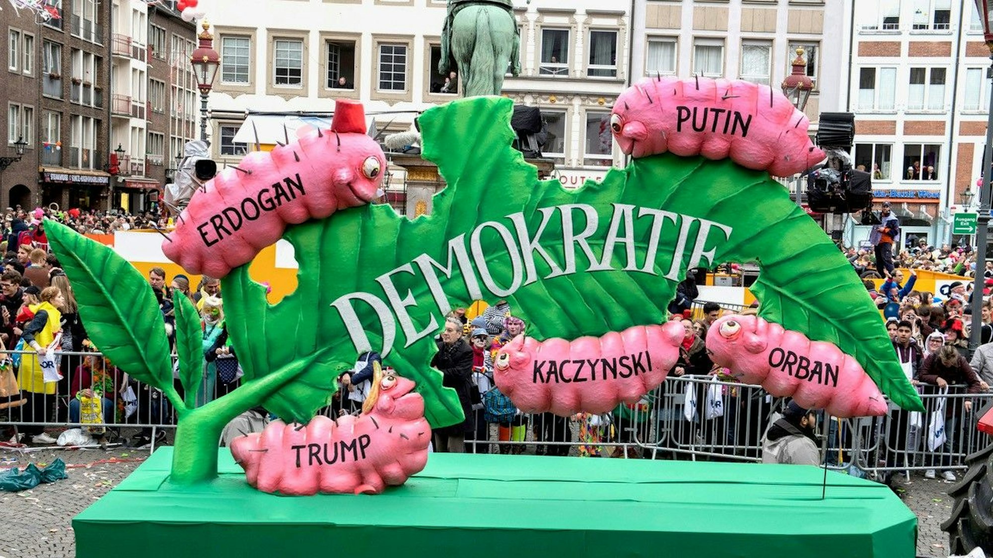 Ein Karnevalswagen bildet ein Blatt mit der Aufschrift Demokratie. Fünf rosa Raupen fressen sie auf. Auf ihnen sind die Name Erdogan, Putin, Trump, Kaczynski und Orban zu lesen.