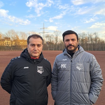 Zwei Männer stehen auf einem Asche-Sportplatz.