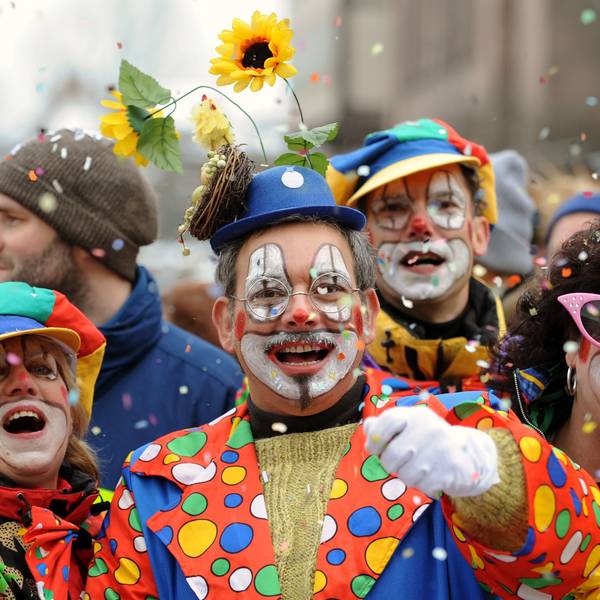 Besucher in Clown-Kostümen werfen bei einem Karnevalsumzug mit Konfetti.