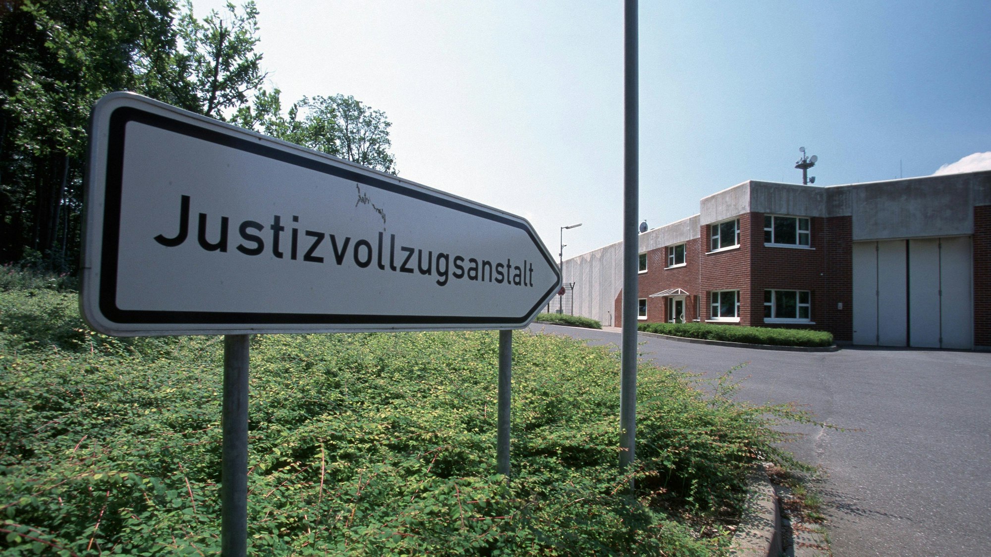 Ein Schild vor der Anstalt zeigt den Weg mit der Aufschrift Justizvollzugsanstalt.