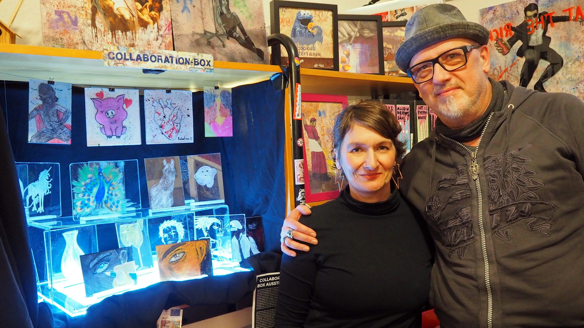 Eine Frau und ein Mann stehen vor Scratchart-Werken.