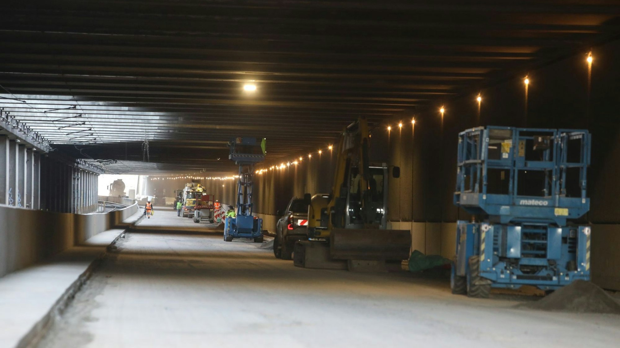 Blick in einen Tunnel, an dessen rechten Rand Baumaschinen und Fahrzeuge stehen.