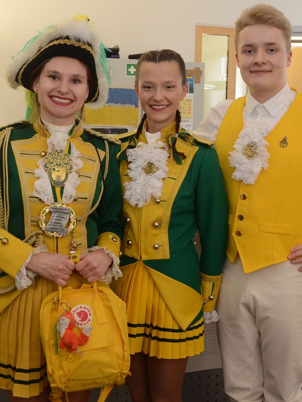 Ein Gardetanzpaar und eine weitere Frau in einer grün-gelben Karnevalsuniform.