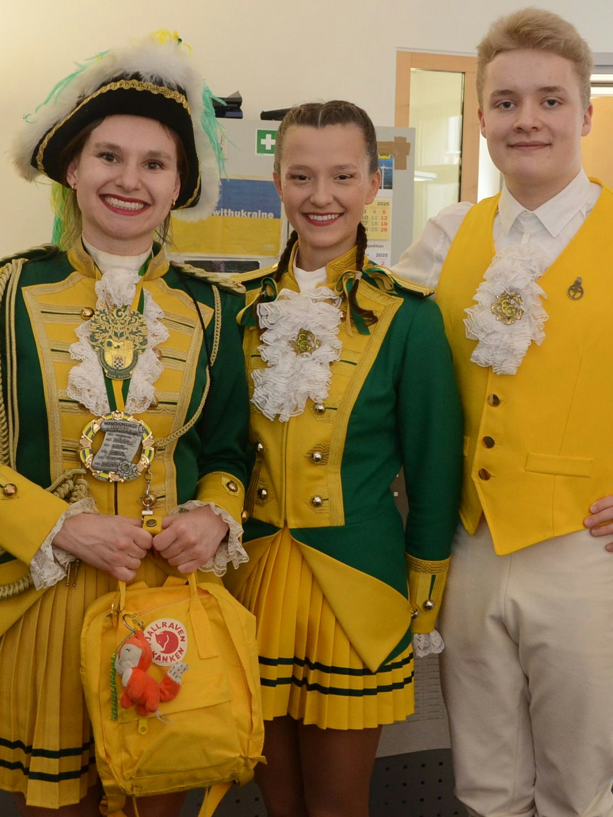 Ein Gardetanzpaar und eine weitere Frau in einer grün-gelben Karnevalsuniform.