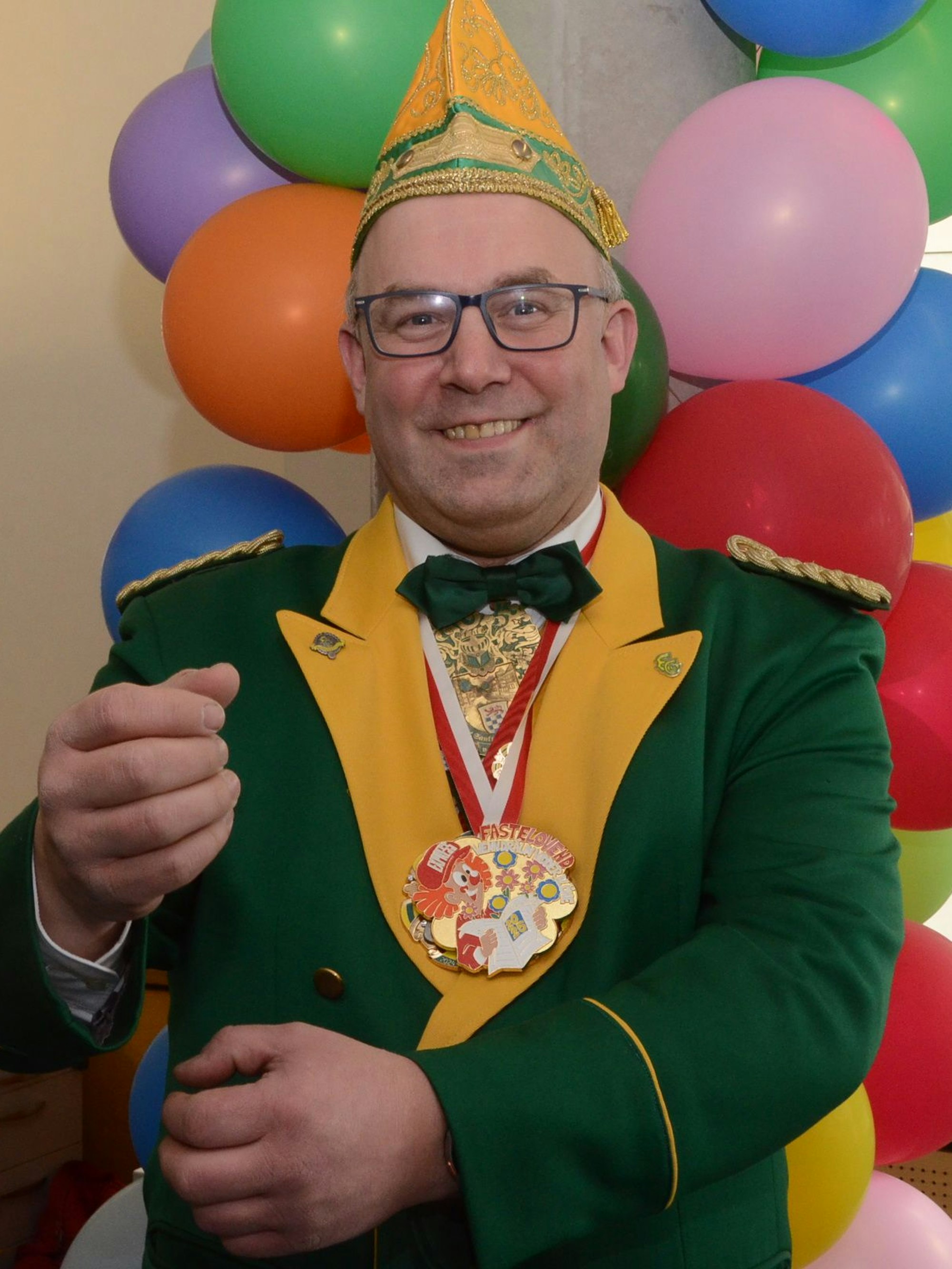 Ein Mann in einer grün-gelben Karnevalsuniform und einer passenden Mütze. Er hält die Hände vor sich, als trage er eine Fahne oder Standarte.