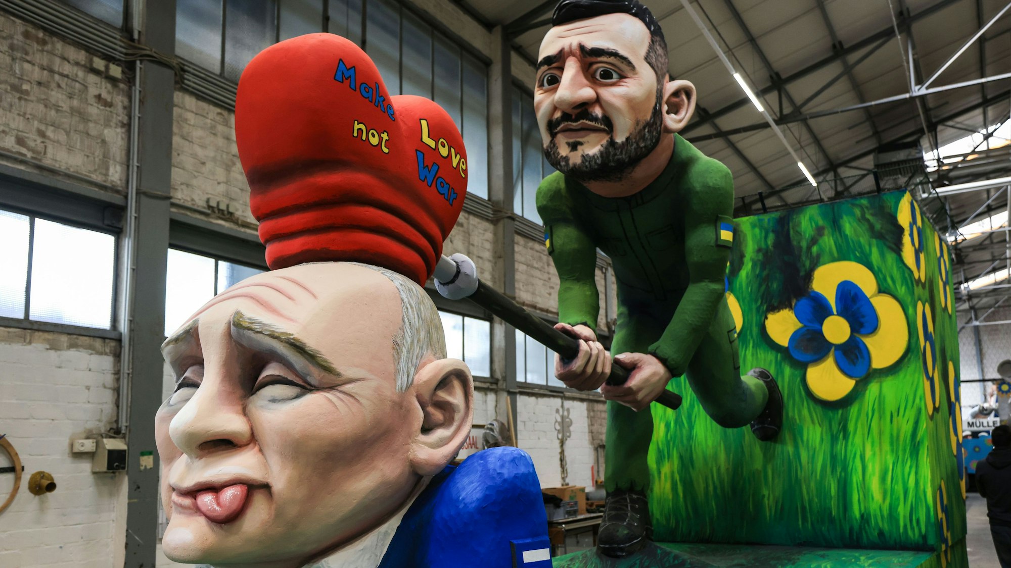 Ein Motivwagen zum Thema Ukraine-Krieg steht beim Richtfest des Kölner Rosenmontagszuges in der Wagenhalle. Eine Selenskyi-Figur haut mit einem „Herzhammer“ auf eine Putin-Figur.