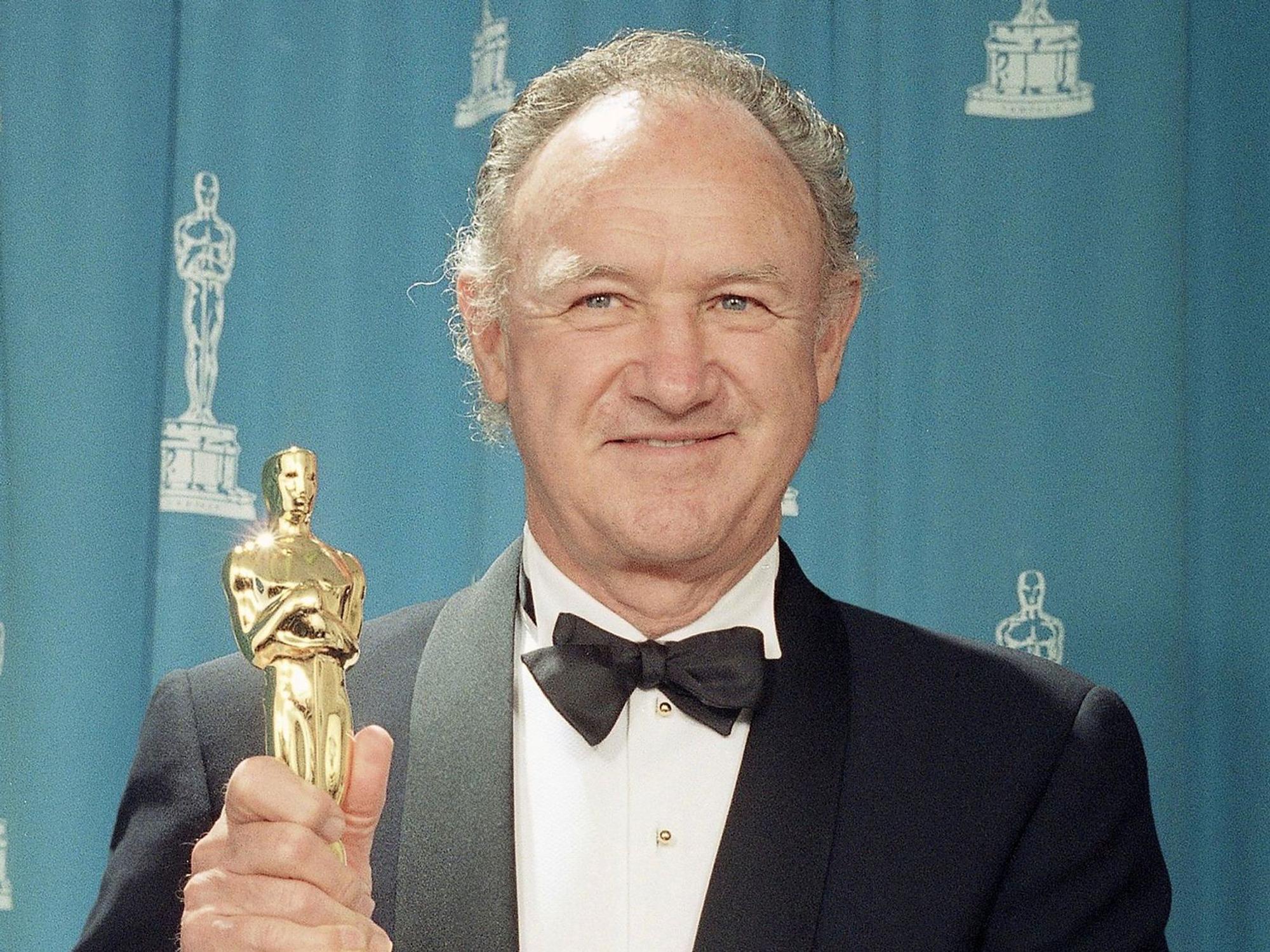 Gene Hackman hält einen Oscar in der Hand und lächelt.