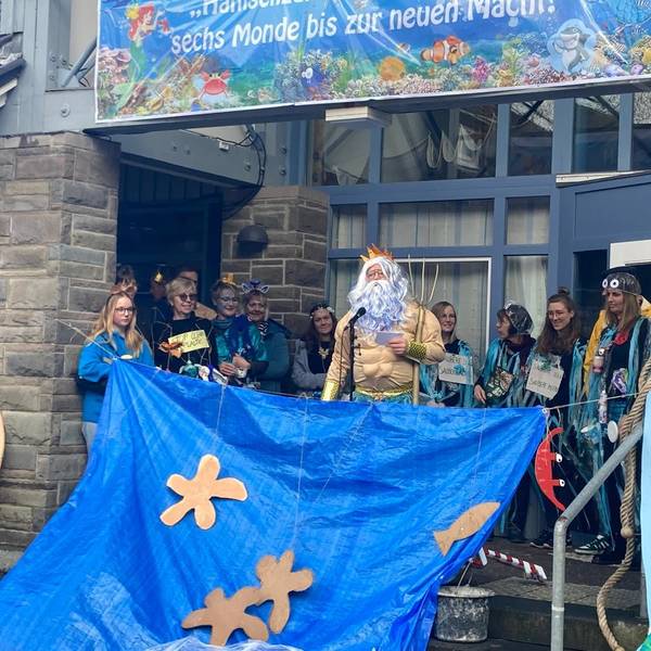 Kürtens Bürgermeister Willi Heider steht im Poseidon-Kostüm vor den Rathaus-Mitarbeitern, die als blaue aquatische Fabelwesen verkleidet sind.