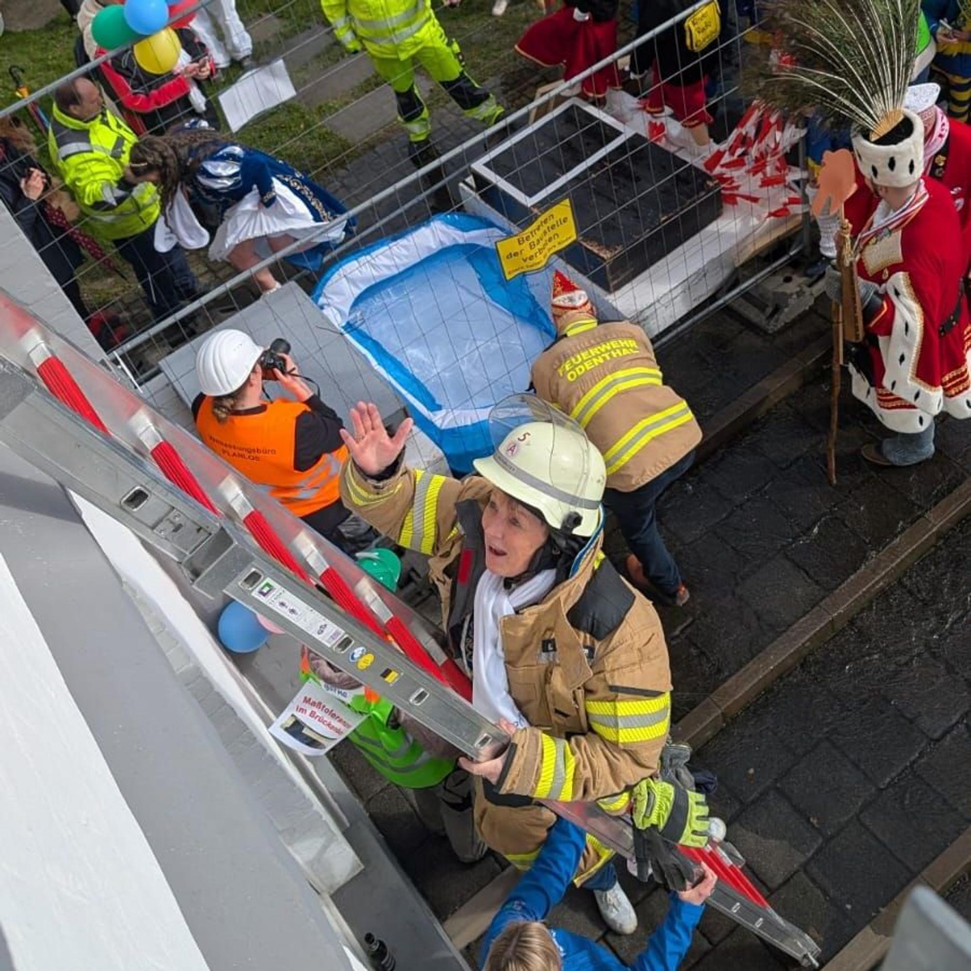 Eine Frau in Feuerwehrausrüstung klettert auf einer Leiter an einer Hauswand empor.