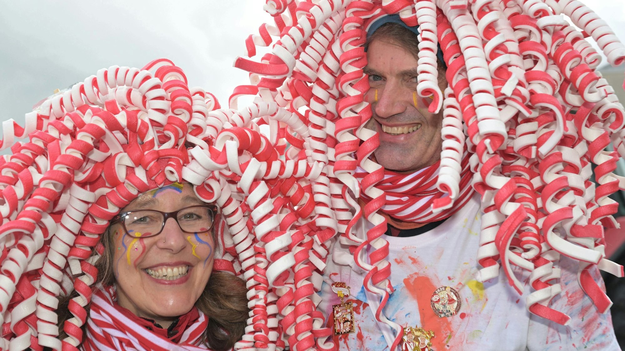 Eine Frau und ein Mann im Malerkostüm mit rot-weißer Perücke lachen in die Kamera.