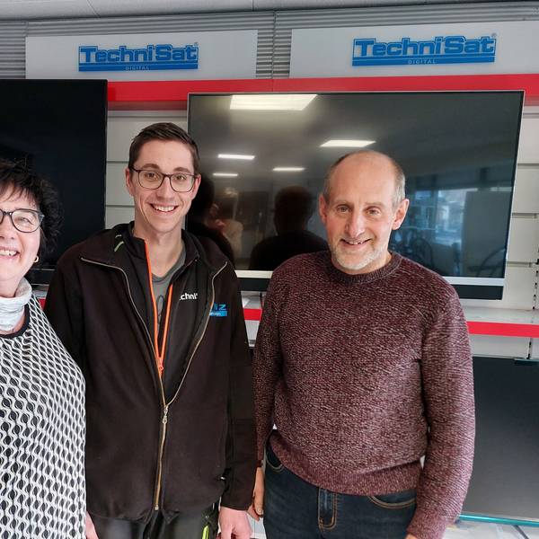 Zwei Männer und eine Frau stehen in einem Geschäft vor ausgestellten Fernsehern in einem Geschäft.