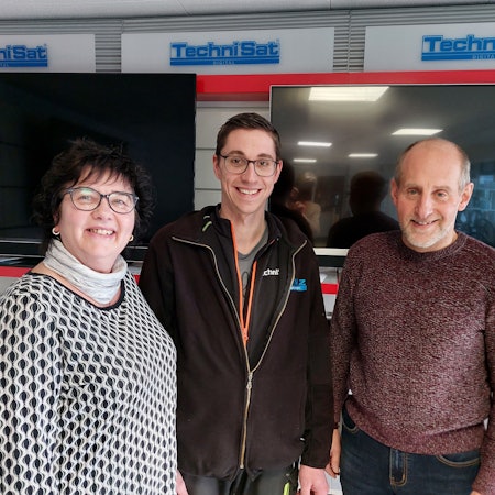 Zwei Männer und eine Frau stehen in einem Geschäft vor ausgestellten Fernsehern in einem Geschäft.