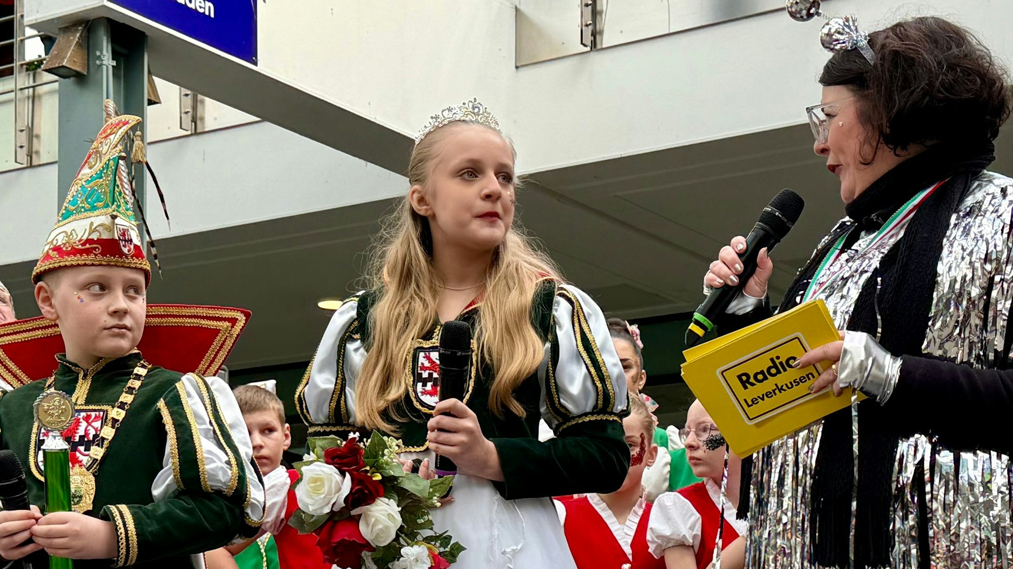 Das Wiesdorfer Kinderprinzenpaar Sophie Rubeque und Lennart Geressen mit Moderatorin Diana Mühlhaus