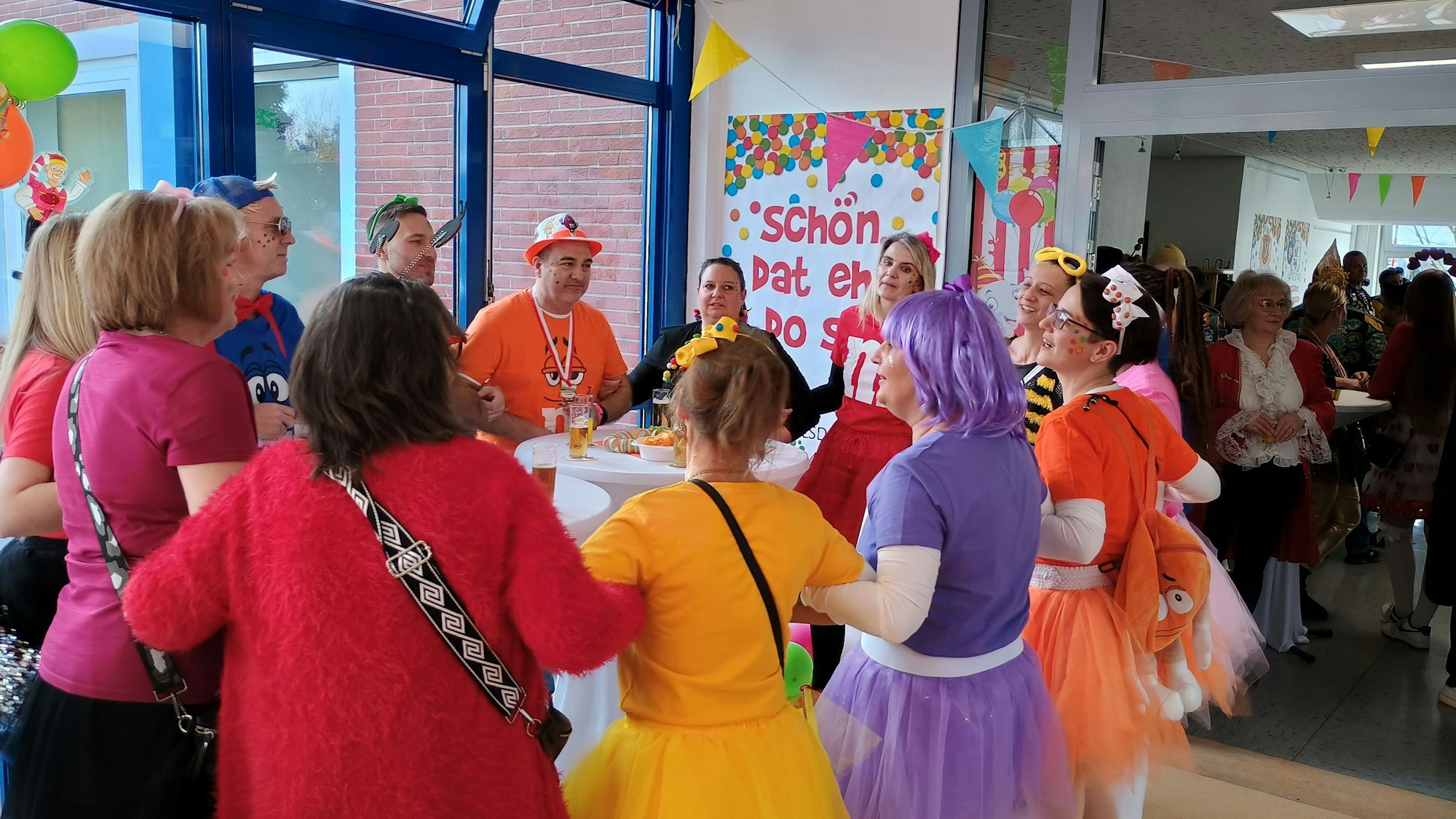 Die Mitarbeitenden halten sich an den Händen und schunkeln. Sie tragen bunte Kostüme.