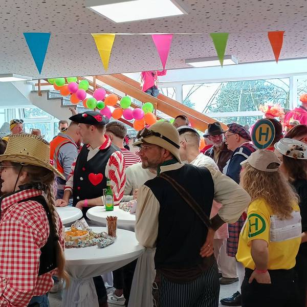 Auf dem Bild sind zahlreiche kostümierte Menschen zu sehen, die um Stehtischen herum stehen.