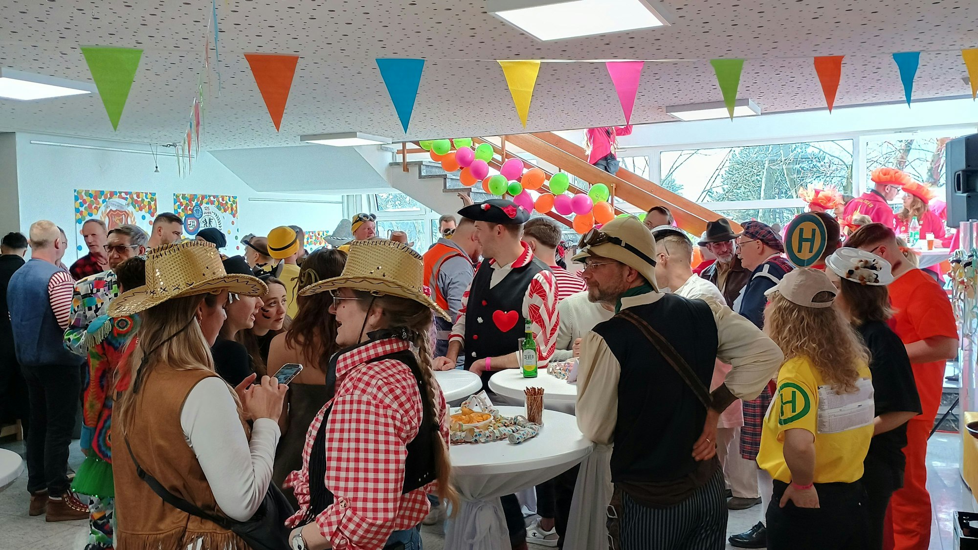 Auf dem Bild sind zahlreiche kostümierte Menschen zu sehen, die um Stehtischen herum stehen.