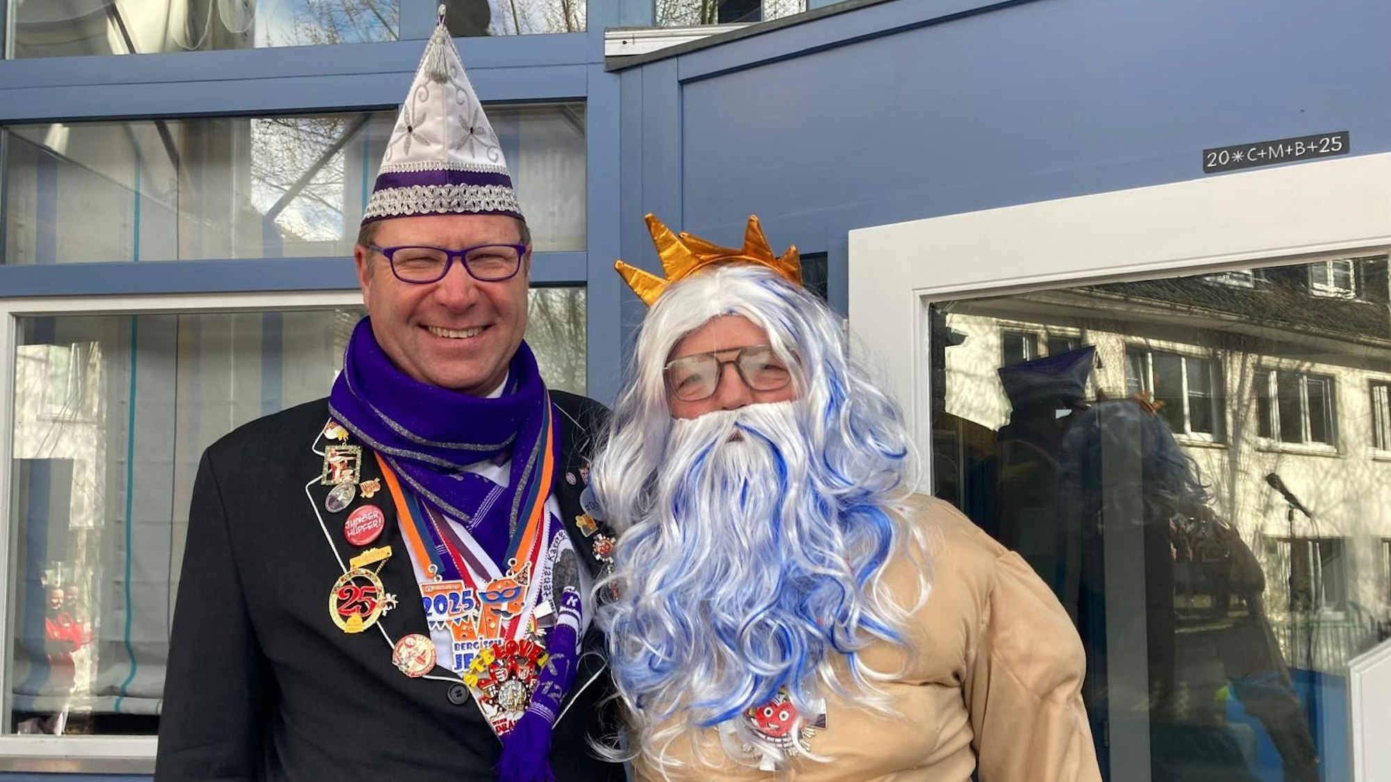 Im Poseidon-Kostüm steht Willi Heider neben Thorsten Kurpjuhn vom Kürtener Karnevalsverein, der einen weißen Hut und einen lilafarbenen Schal trägt.