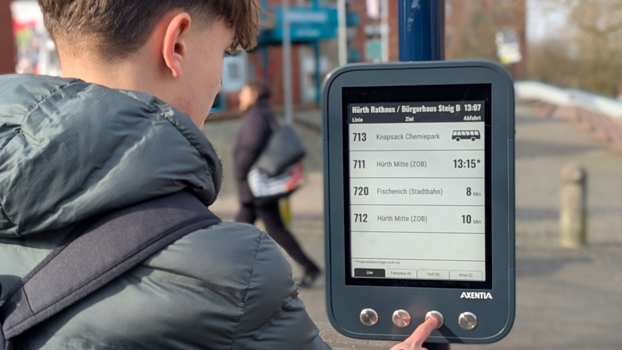 Zu sehen ist ein Jugendlicher, der eine digitale Anzeigetafel an einer Bushaltestelle bedient.