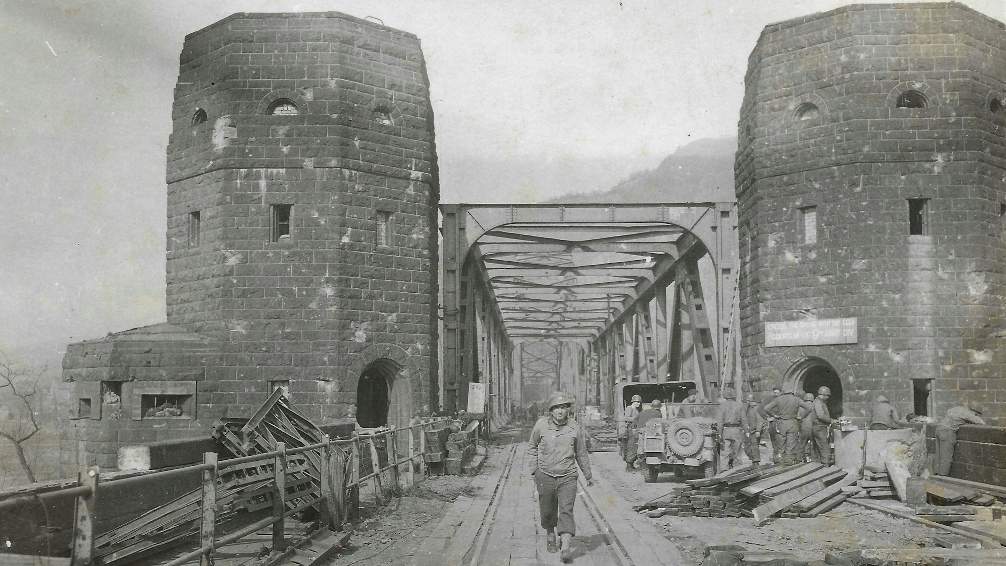 Eine historische Aufnahme, auf der ein Soldat zwischen den Türmen der Brücke von Remagen hindurch geht.