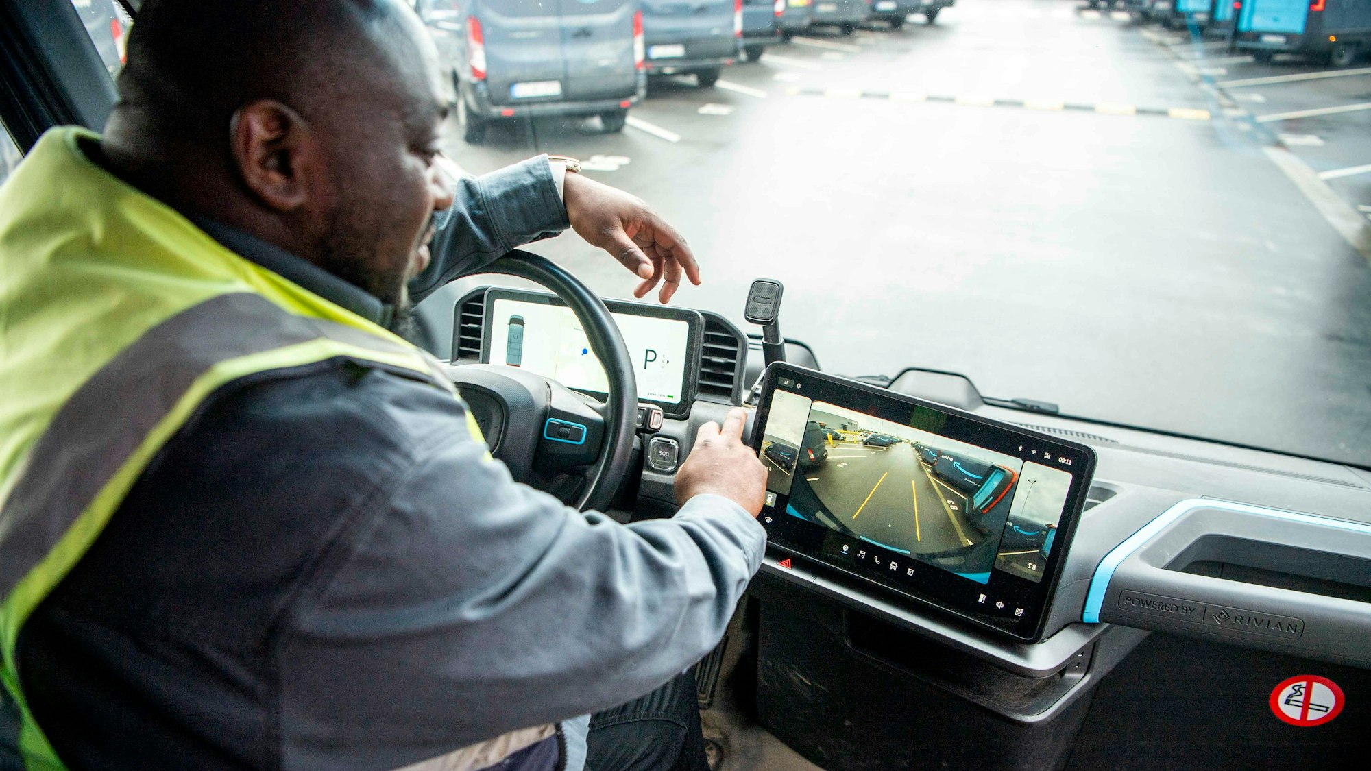 Ein Fahrer trägt eine gelbe Warnweste über der Jacke und startet im Amazon-Verteilzentrum in Euskirchen einen E-Transporter.