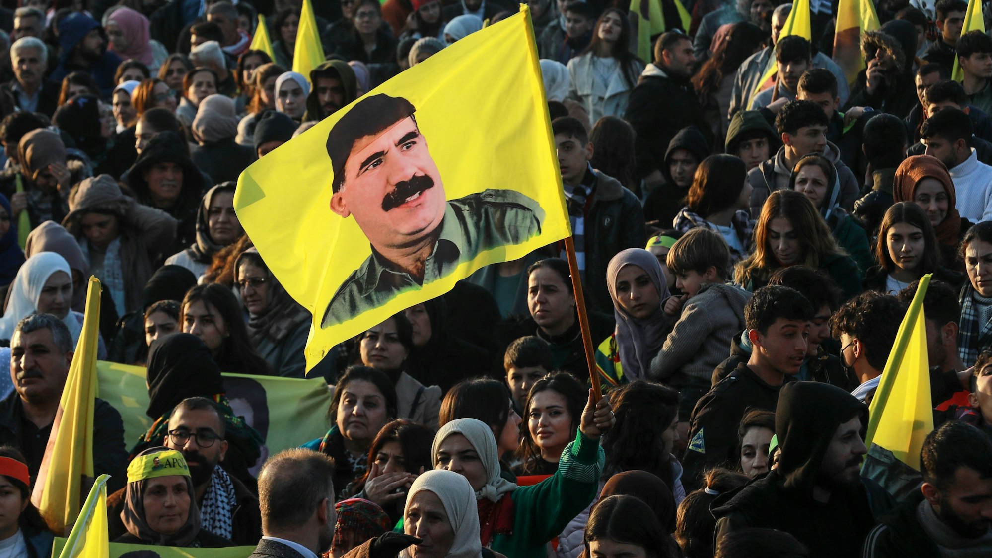 Eine kurdisch-syrische Frau schwenkt in einer Menschenmenge eine Fahne mit dem Konterfei Abdullah Öcalans.