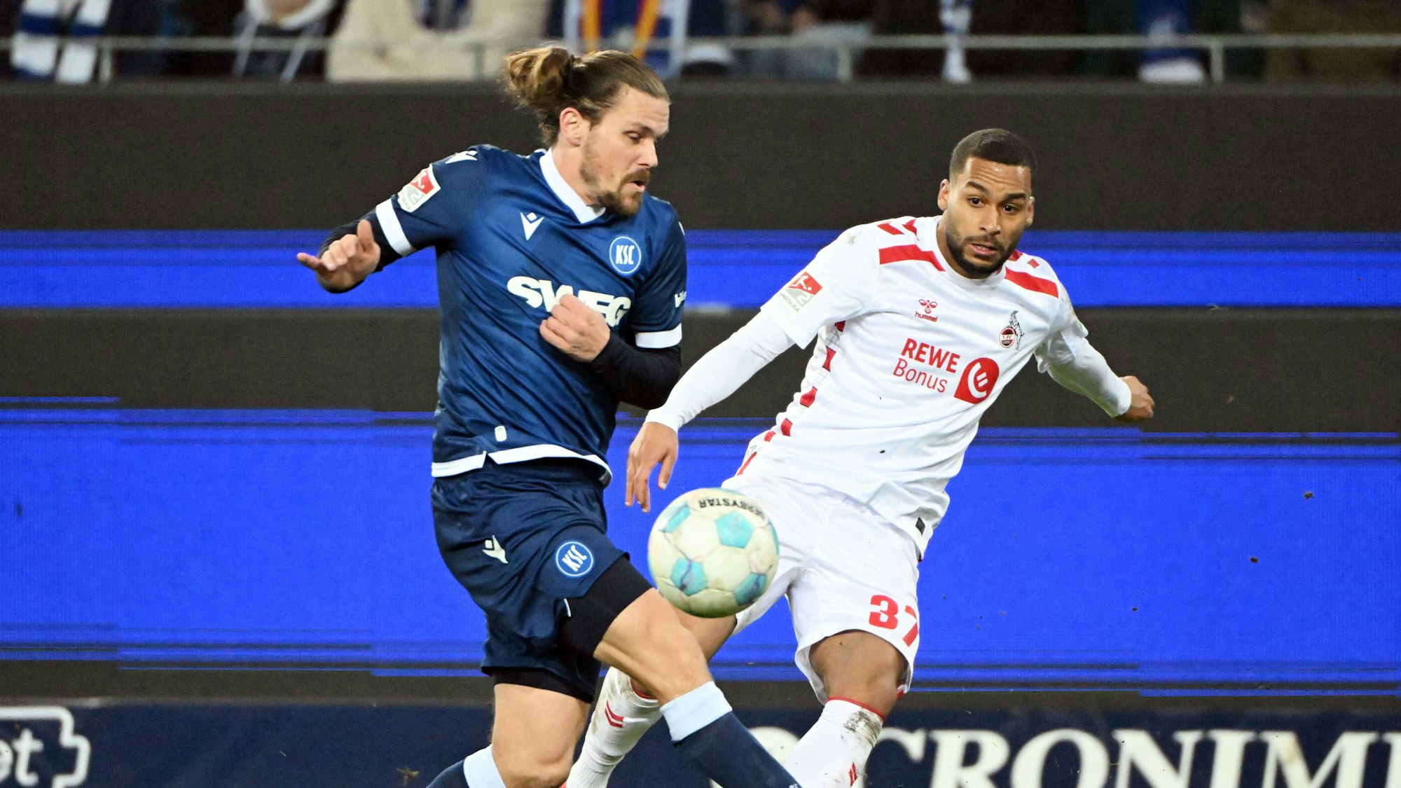 01.03.2025, Baden-Württemberg, Karlsruhe: Fußball: 2. Bundesliga, Karlsruher SC - 1. FC Köln, 24. Spieltag, BBBank Wildpark. Der Karlsruher Sebastian Jung (l) und der Kölner Linton Maina kämpfen um den Ball. Foto: Uli Deck/dpa - WICHTIGER HINWEIS: Gemäß den Vorgaben der DFL Deutsche Fußball Liga bzw. des DFB Deutscher Fußball-Bund ist es untersagt, in dem Stadion und/oder vom Spiel angefertigte Fotoaufnahmen in Form von Sequenzbildern und/oder videoähnlichen Fotostrecken zu verwerten bzw. verwerten zu lassen. +++ dpa-Bildfunk +++