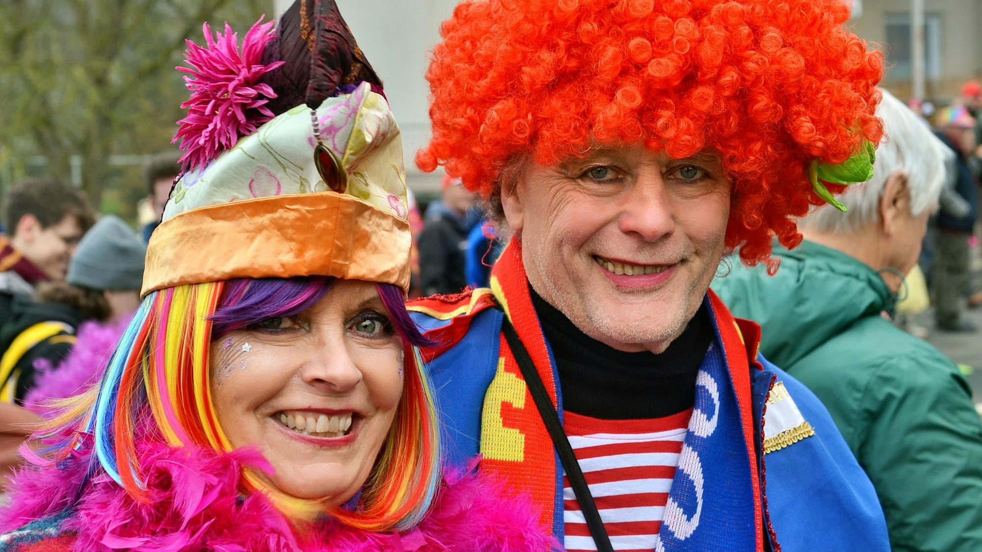 Zwei bunt kostümierte Jecke, eine Frau mit pinker Federboa und bunter Perücke und ein Mann mit roter Perücke, feierten den Eicherscheider Karnevalszug.