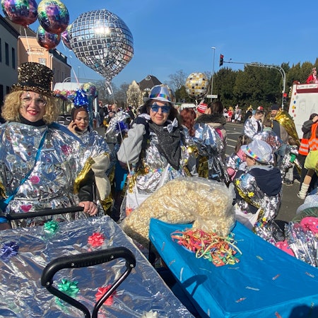 Frauen in silberglänzenden Kostümen schieben Bagagewagen.