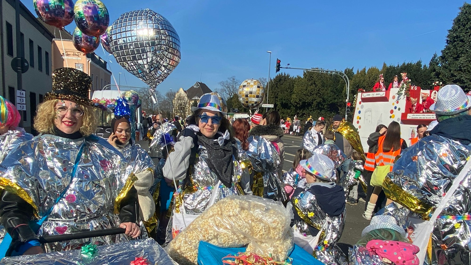Frauen in silberglänzenden Kostümen schieben Bagagewagen.