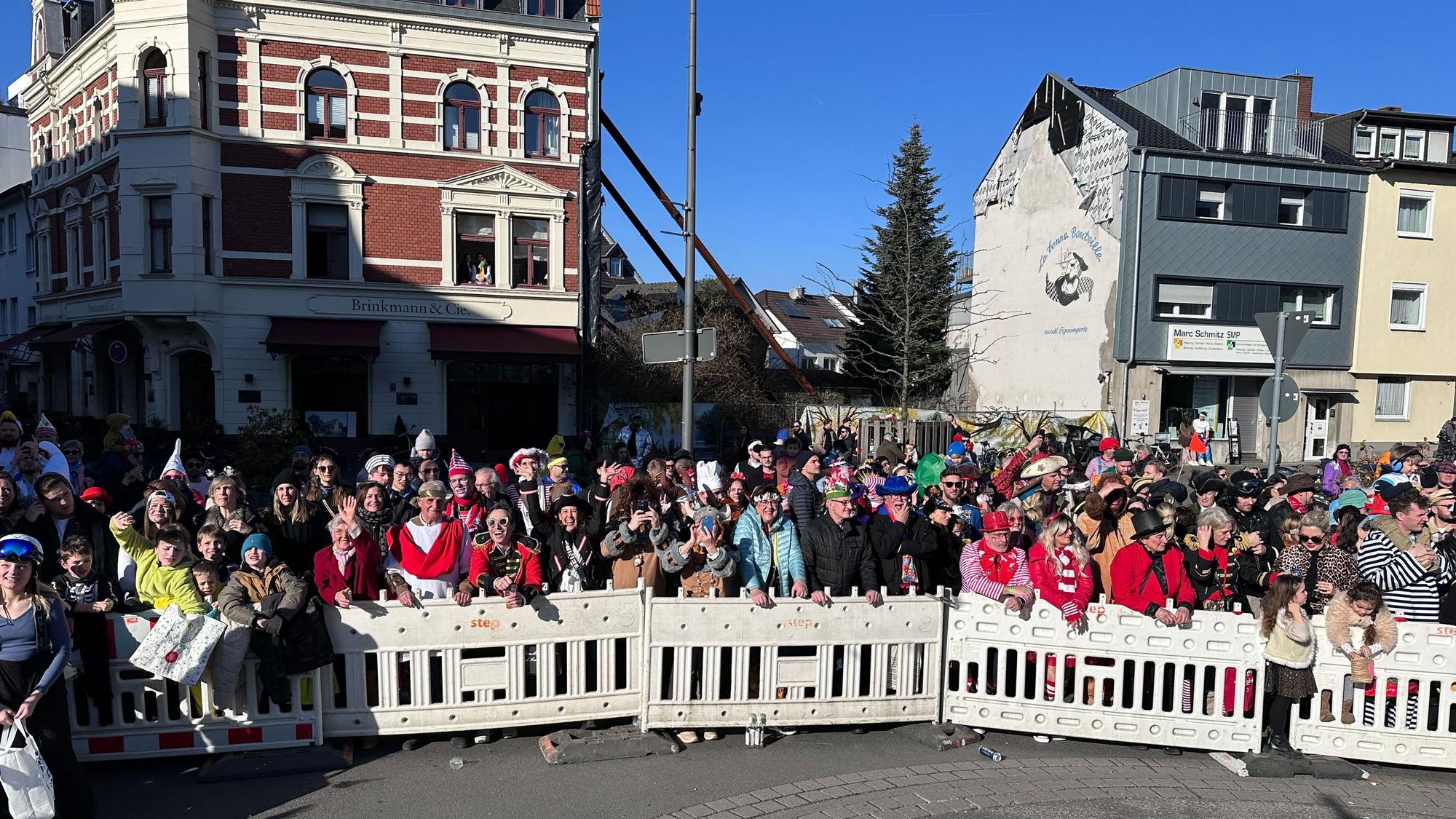 Hinter einer Absperrung stehen verkleidete Menschen am Rande des Zugwegs in Rodenkirchen.