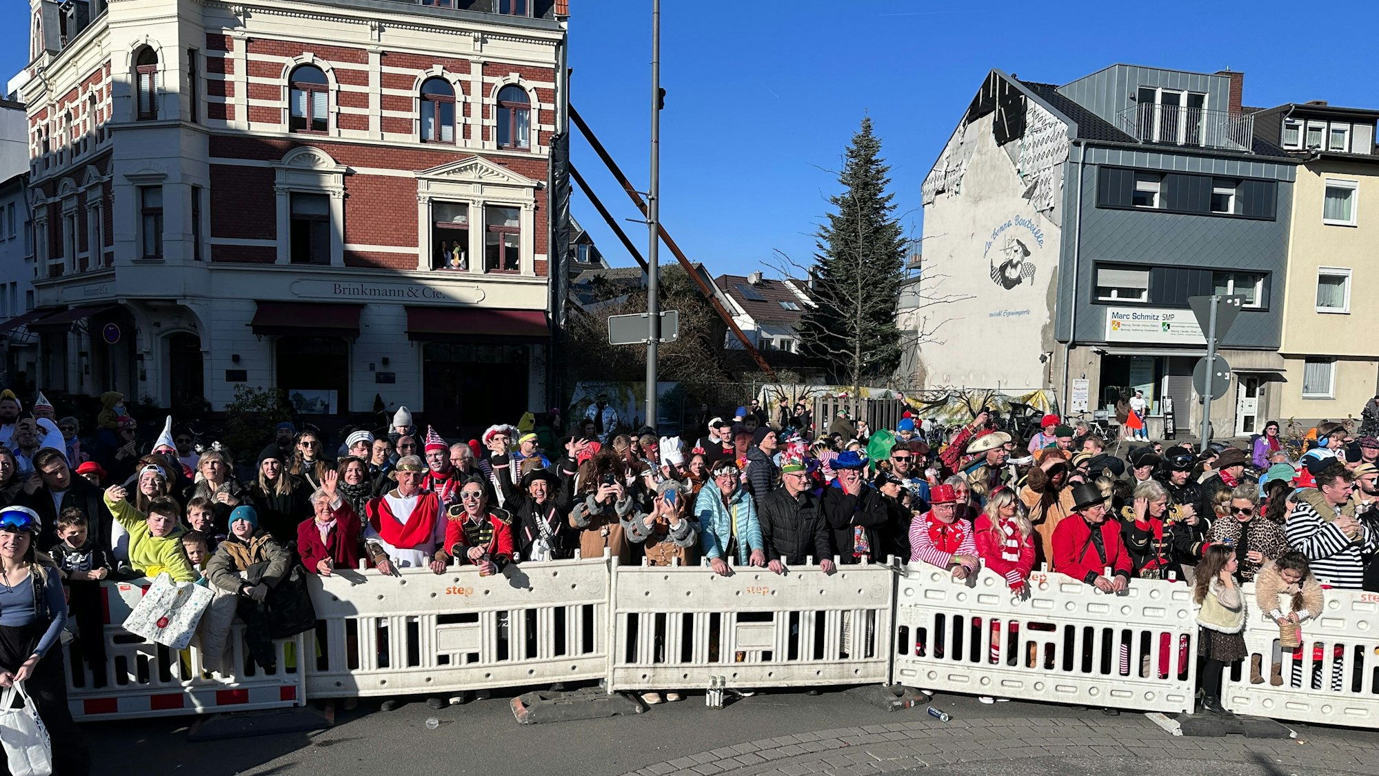 Hinter einer Absperrung stehen verkleidete Menschen am Rande des Zugwegs in Rodenkirchen.