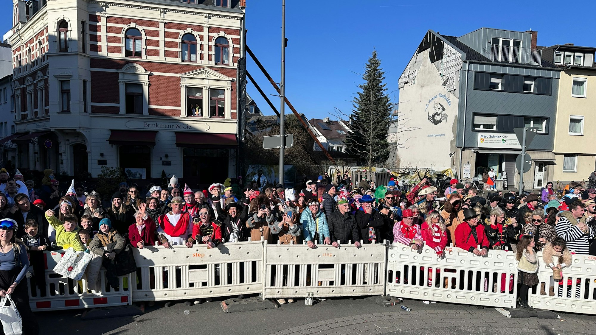 Hinter einer Absperrung stehen verkleidete Menschen am Rande des Zugwegs in Rodenkirchen.