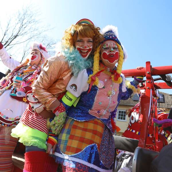 Drei bunt kostümierte und geschminkte Frauen als Clowns auf einem Karnevalswagen.