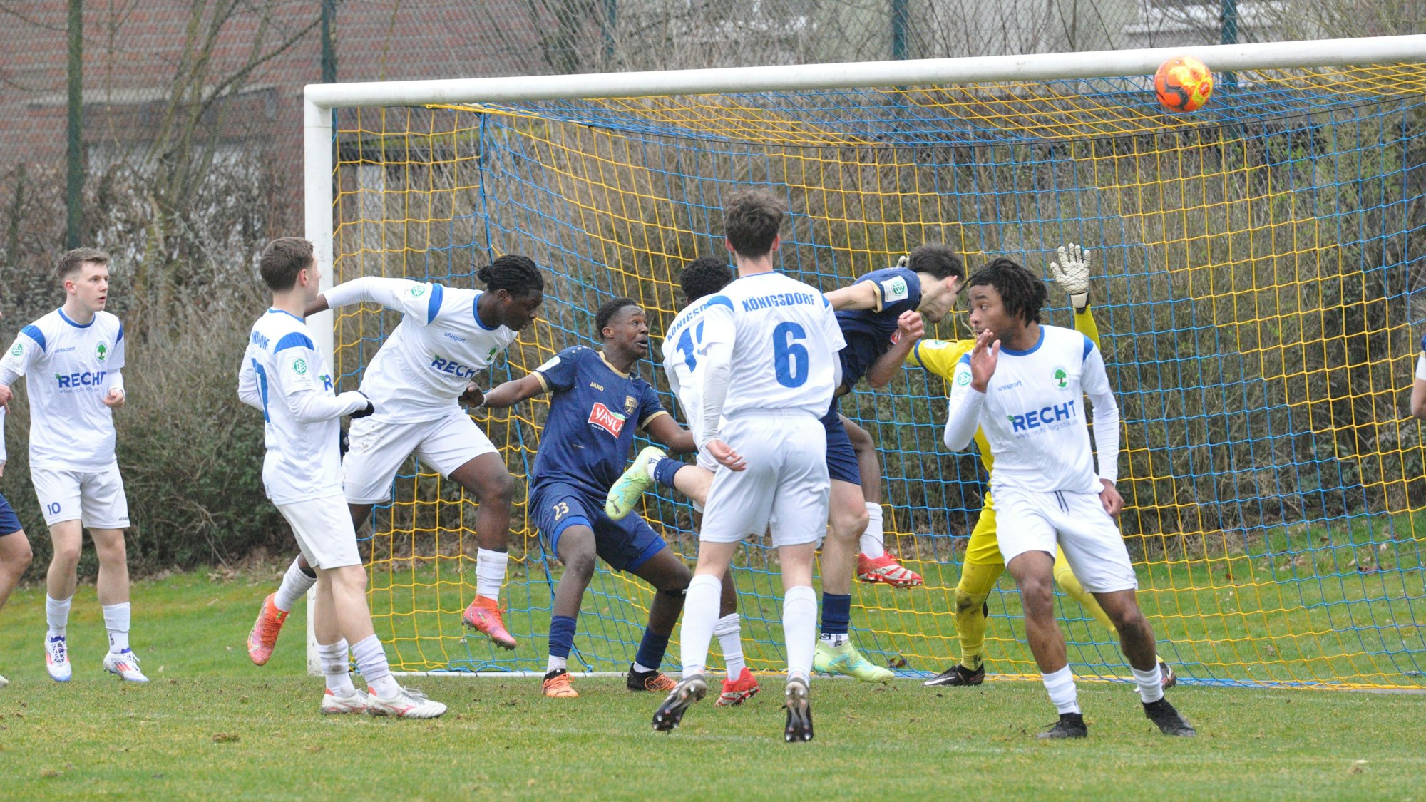 Das Foto zeigt eine Spielertraube vor dem Tor der Königsdorfer, aus der ein blau gekleideter Meerbuscher die Führung köpft.