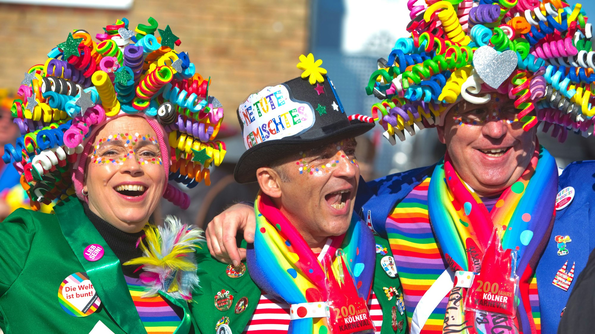 Drei bunt kostümierte jecke bei einem Karnevalszug.
