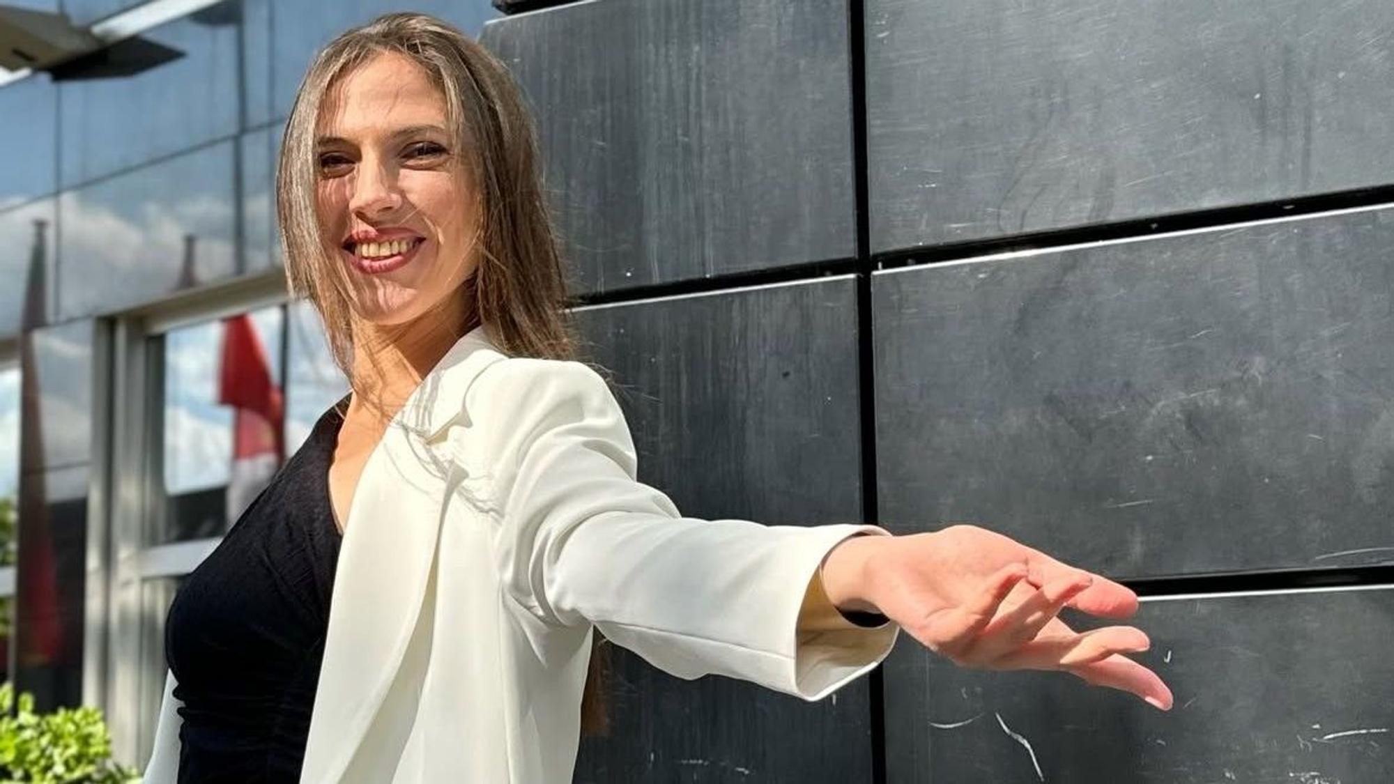 Auf dem Foto ist eine Frau zu sehen. Sie hat langes braunes Haar und breitet die Arme aus.