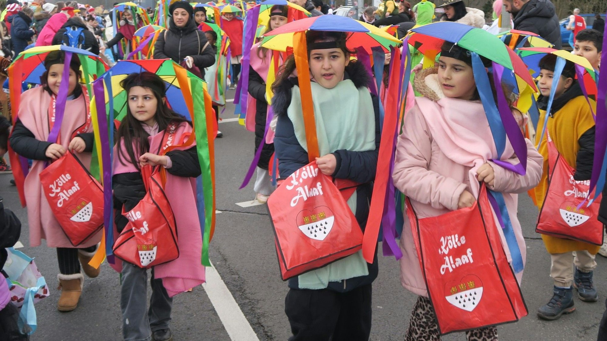 Kinder laufen im Zug mit, sie haben Regenschirmhüte mit langen bunten Bändern daran auf dem Kopf.