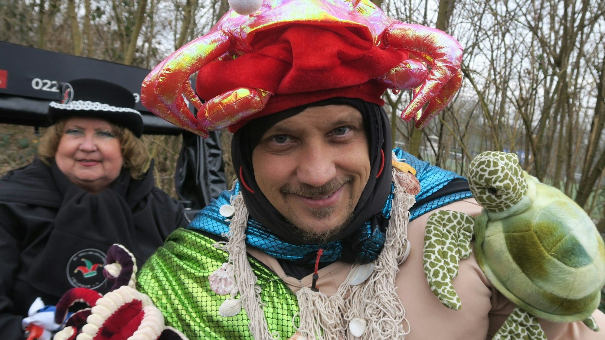 Ein Mann im Fischernetz und einer Qualle auf dem Kopf schaut in die Kamera.