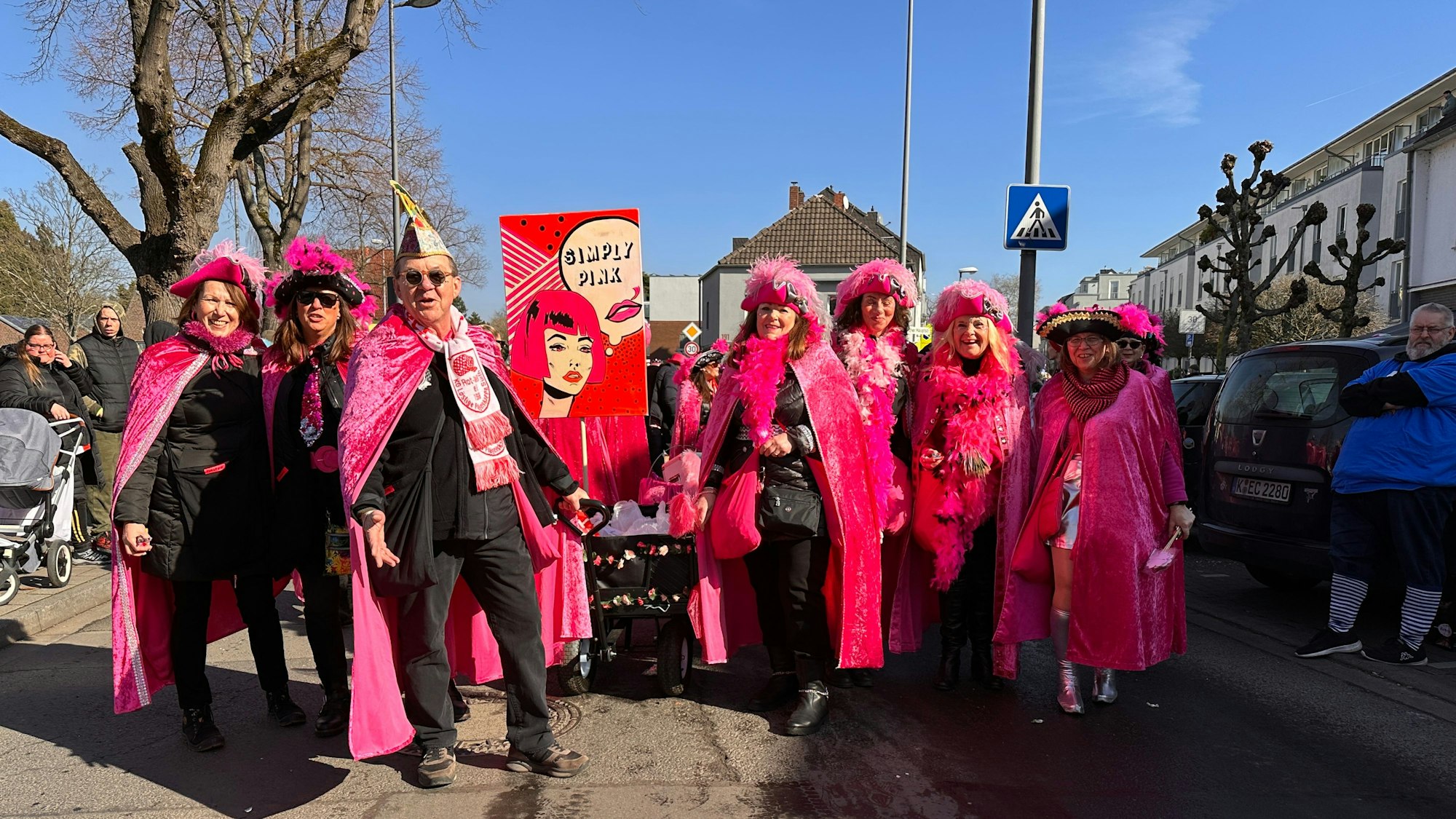 Eine Gruppe Frauen und ein Mann sind in pinken Umhängen und Piratenhüten mit pinken Federn unterwegs.
