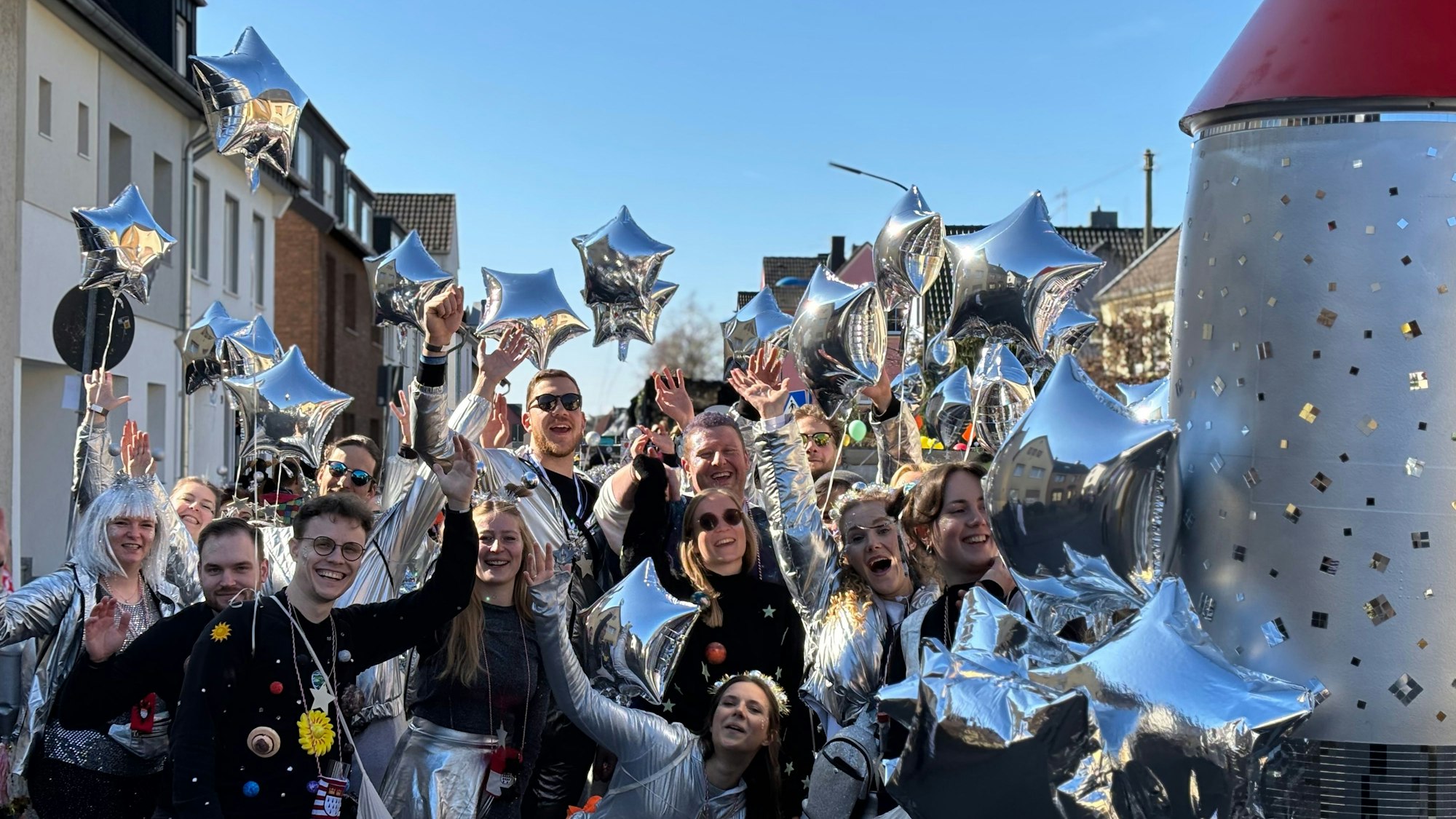 Eine Gruppe Kostümierter im Weltall-Look streckt freudig die Arme nach oben.