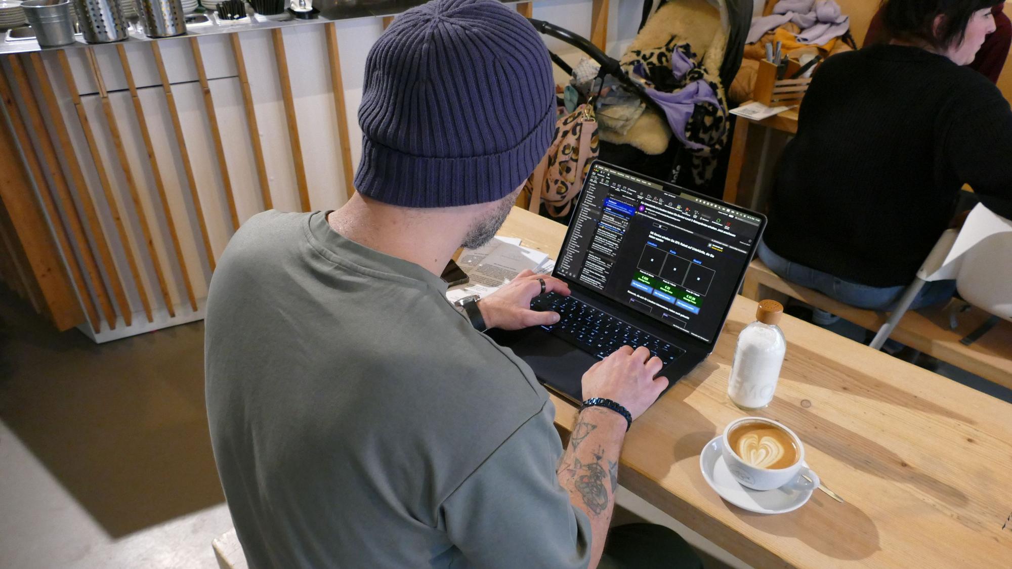 Ein Mann sitzt vor seinem Laptop, neben ihm steht eine Tasse Kaffee.