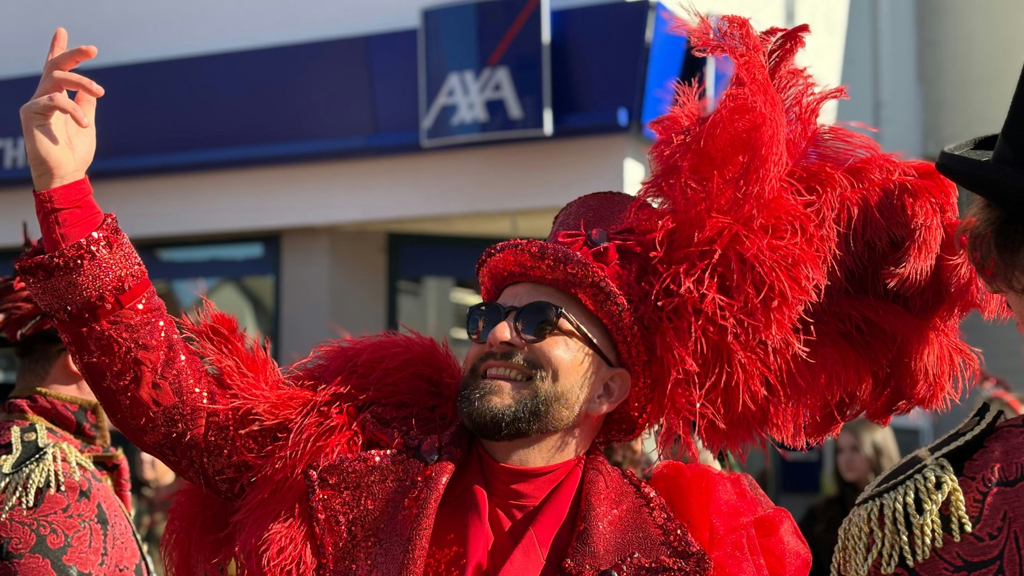 Ein Mann im roten Anzug streckt eine Hand von sich und posiert grinsend für ein Foto.