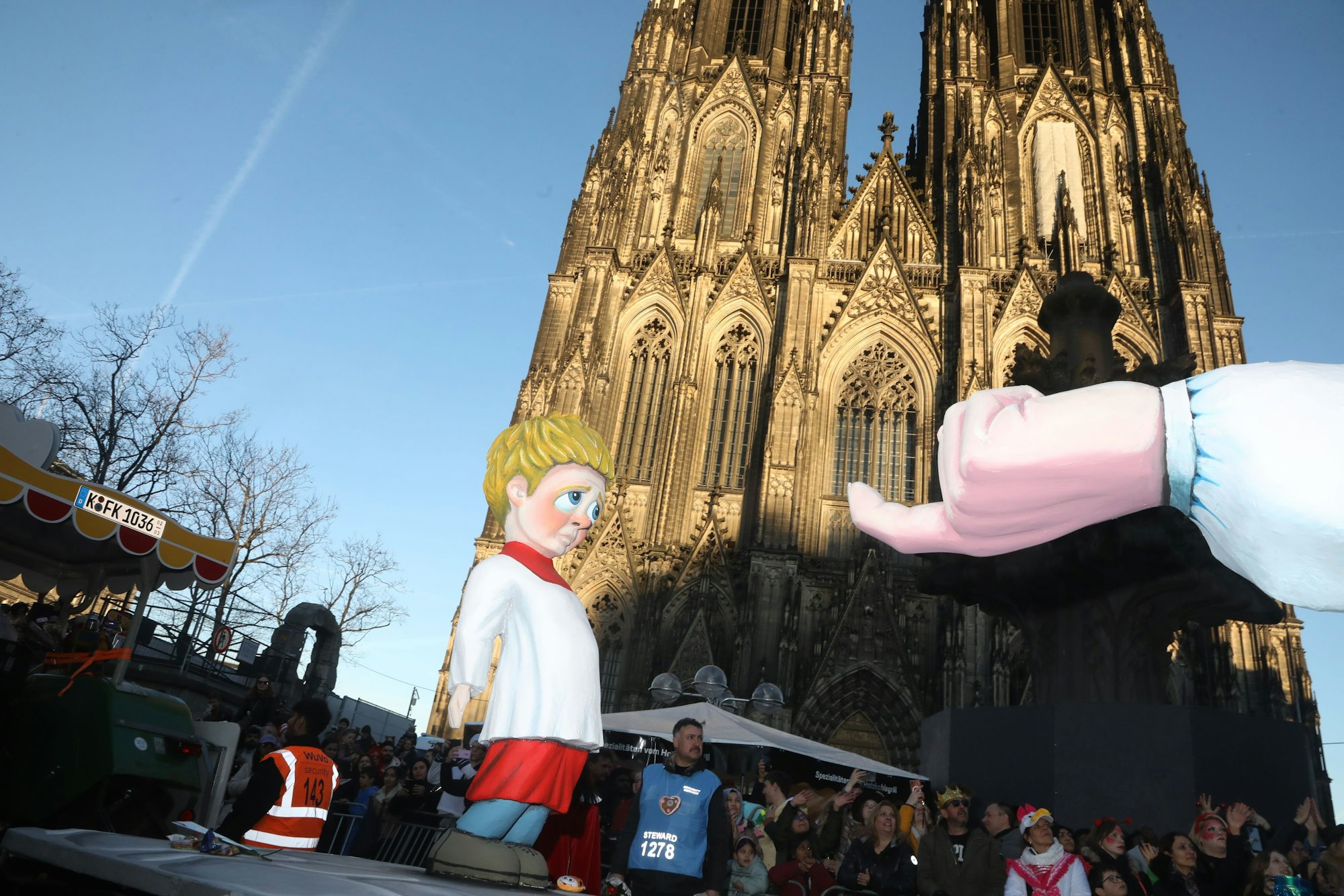 Der umstrittene Persiflagewagen mit der Aufschrift „Jesus liebt dich“ fährt am Kölner Dom vorbei.
