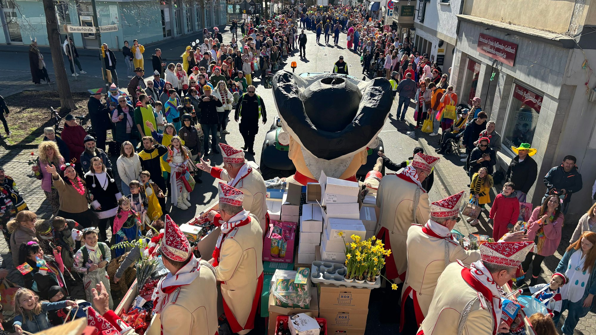 Blick vom Zugwagen der 1. Mondorfer Ehrengarde: An den Straßenrändern stehen verkleidete Zugbesucher und -besucherinnen.