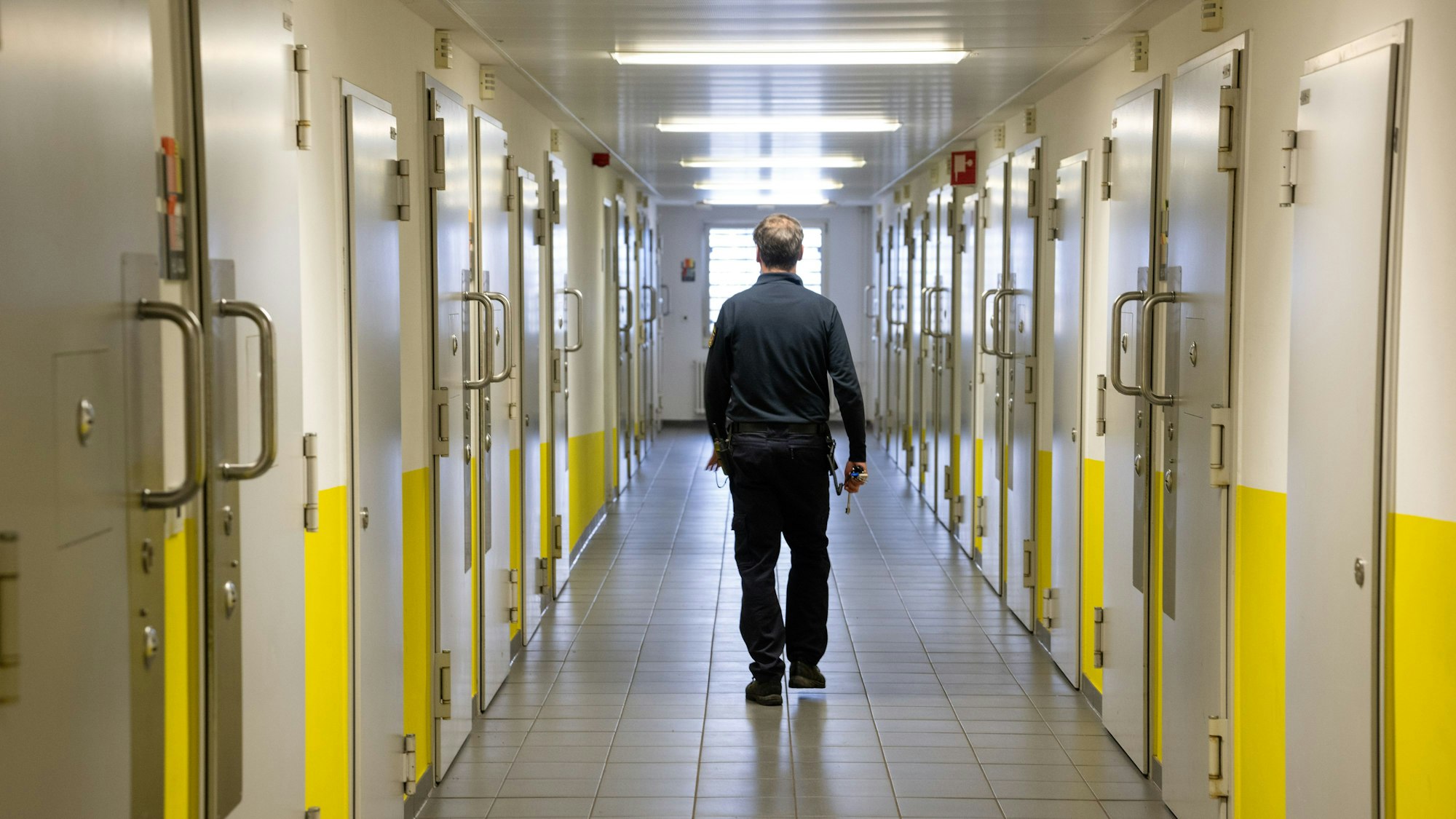 Ein Justizvollzugsbeamter geht durch einen Gang vorbei an den Gefängniszellen. Viele Straftäter kommen in NRW schon schnell in den offenen Vollzug.