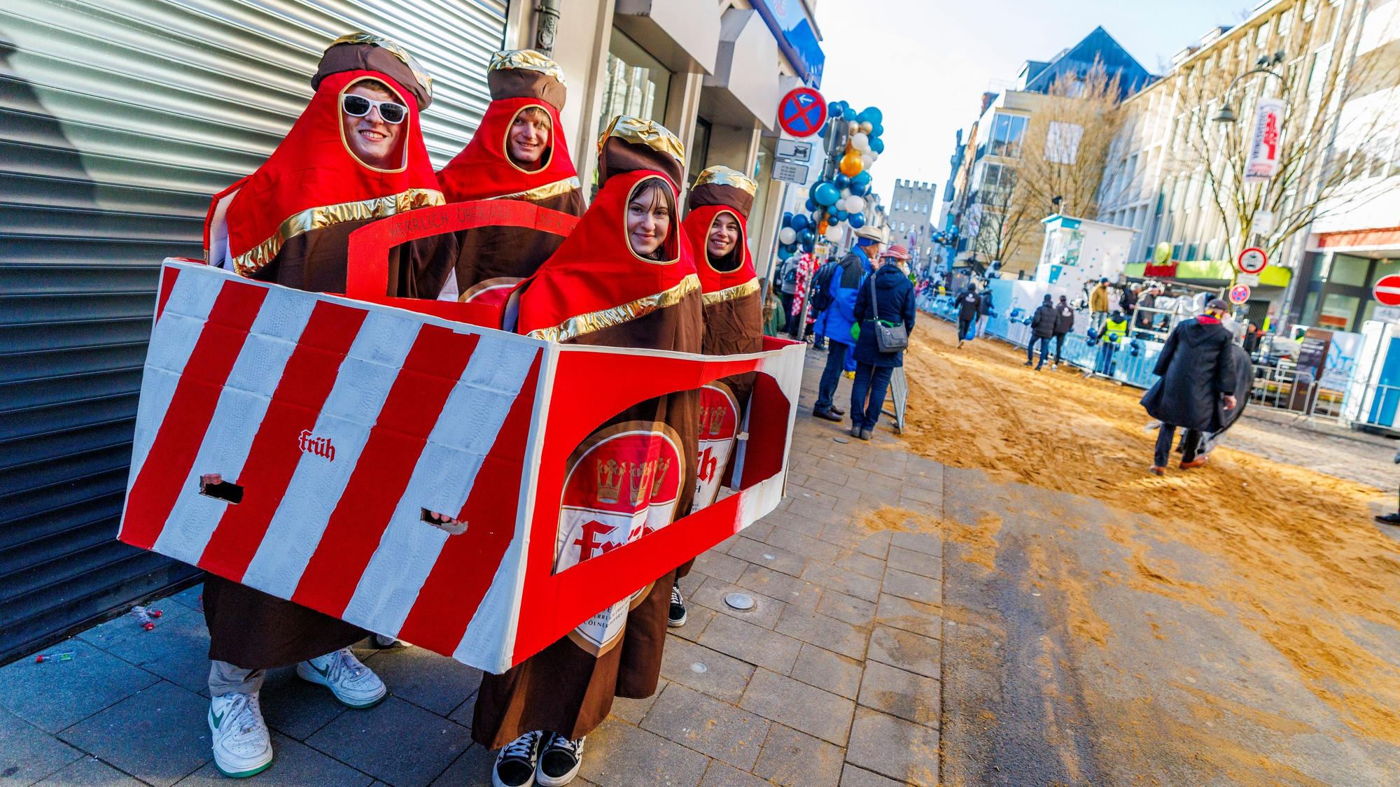 Vier Freunde, verkleidet als Bierkasten, stehen an der Zugstrecke an der Severinstraße.