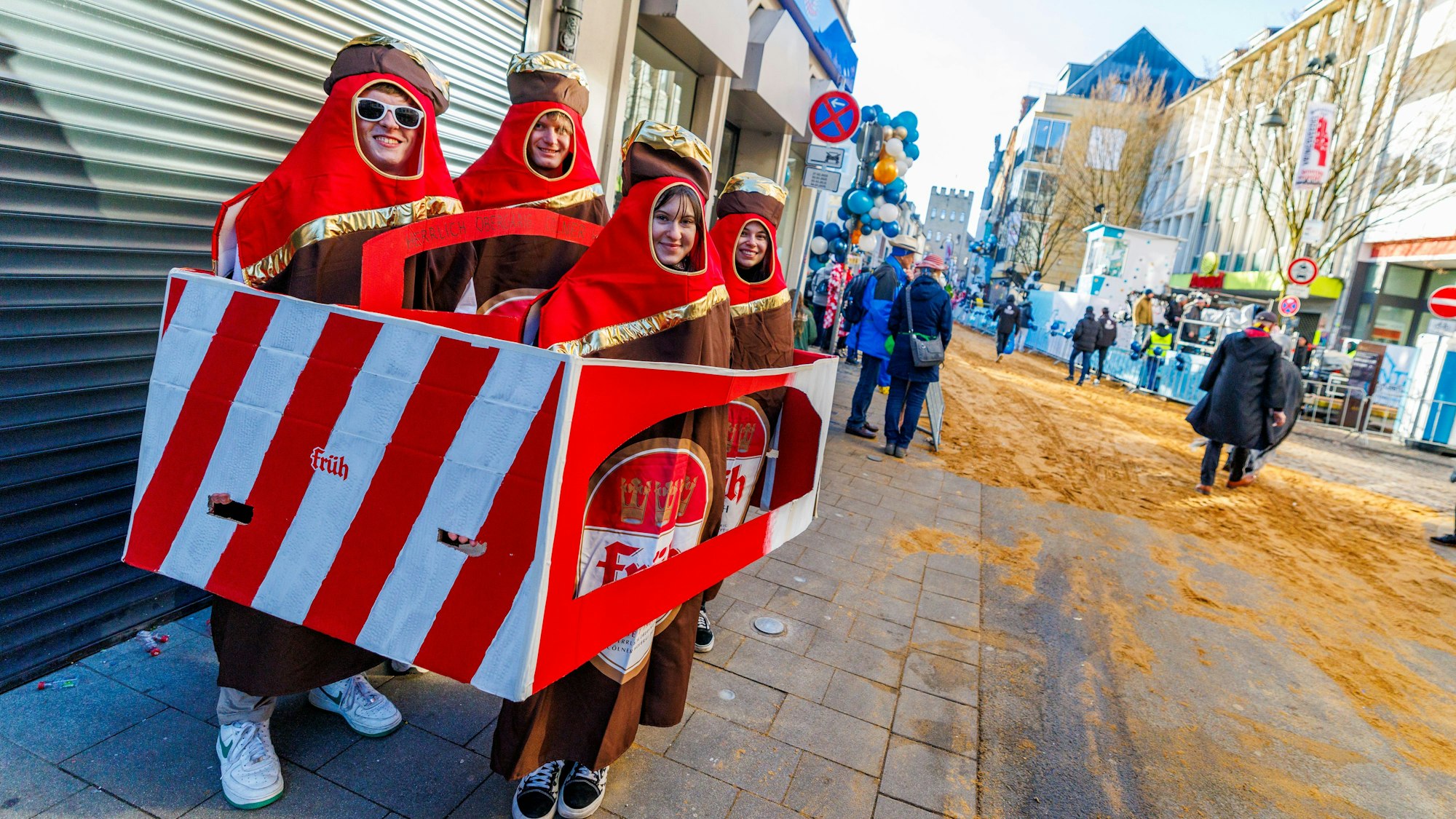Vier Freunde, verkleidet als Bierkasten, stehen an der Zugstrecke an der Severinstraße.